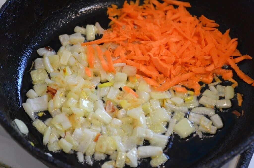 Лук и морковь очистим. Лук измельчим ножом, а морковь пропустим через среднюю тёрку. На растительном масле начала обжарим лук до золотистого цвета, а после добавим морковь и жарим 2 минуты.
