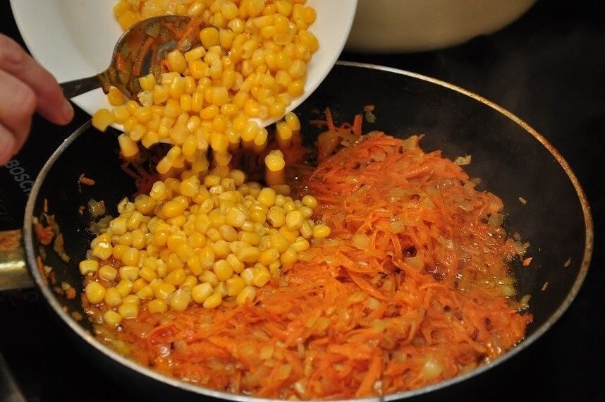 Сливаем с кукурузы жидкость. Лук очистим и измельчим при помощи ножа. Морковку пропускаем через мелкую тёрку. На смазанную растительным маслом сковороду отправим лук, а затем добавим морковь. Тушим и добавляем кукурузу. Тщательно всё перемешаем.