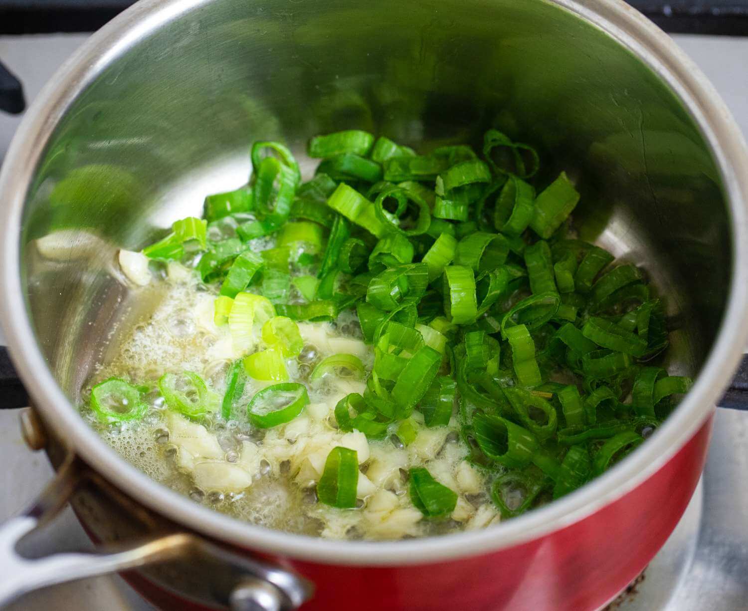 Мелко нарубить чеснок и зеленый лук. Обжарить в сливочном масле примерно 1 минуту.