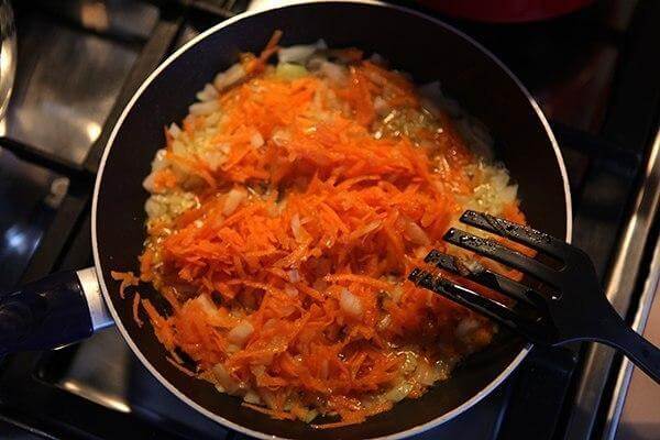Тем временем, очистим лук и морковь. Лук мелко нарежем, а морковь пропустим через среднюю тёрку. На сковороде разогреем масло, обжарим до золотистого цвета лук, а следом добавим морковь. Отправим в суп и доводим до кипения.